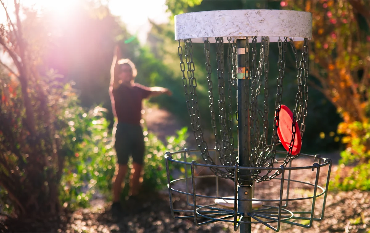 Lány frizbit dob a discgolf kosár felé az őszi parkban