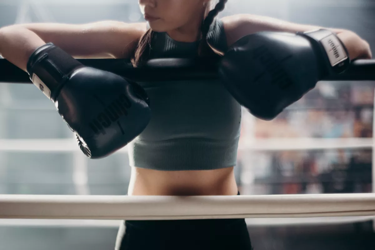 Boxkesztyűs nő a boxring köteleinek támaszkodva pihen edzés közben