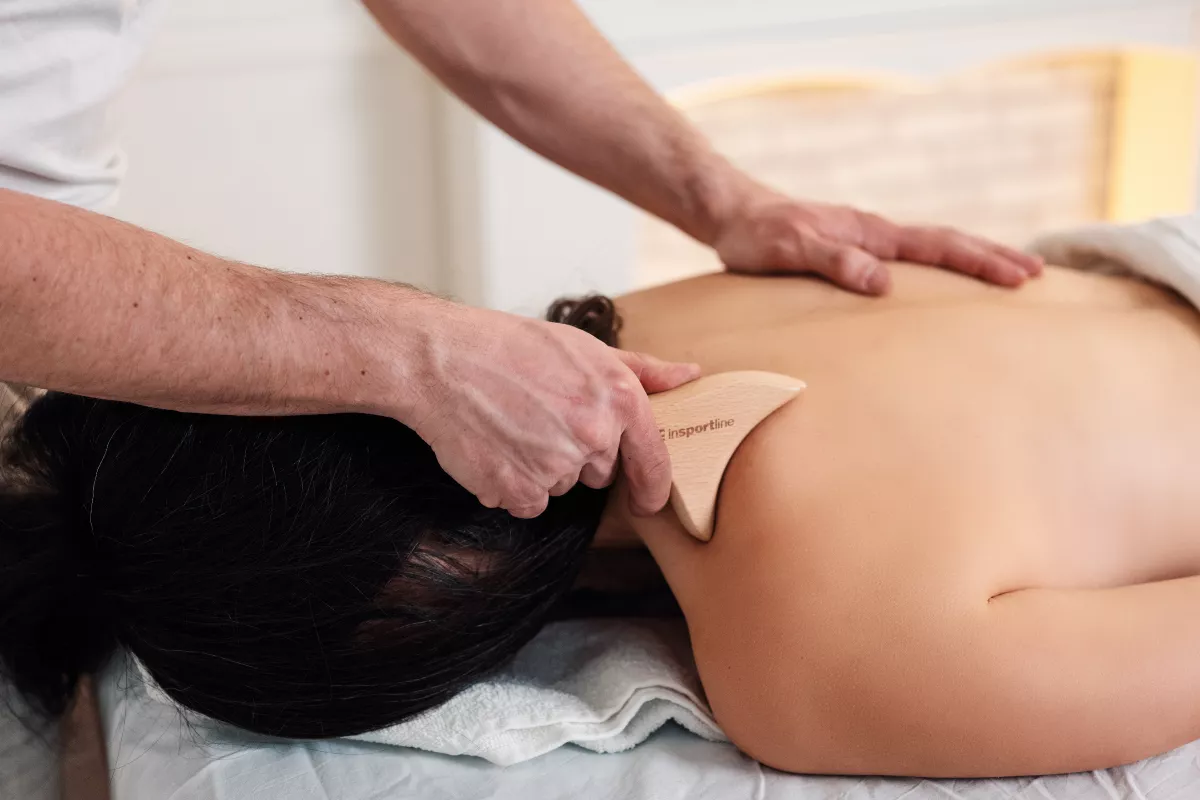 Egy terapeuta fa inSPORTline maderoterápiás eszközzel masszírozza egy nő hátát és vállát