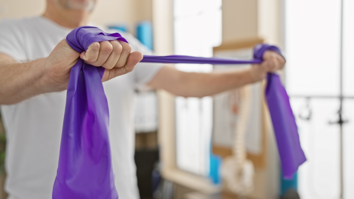 Férfi lila fitness gumiszalagot feszít ki a felsőtest és a testtartást támogató izmok edzéséhez