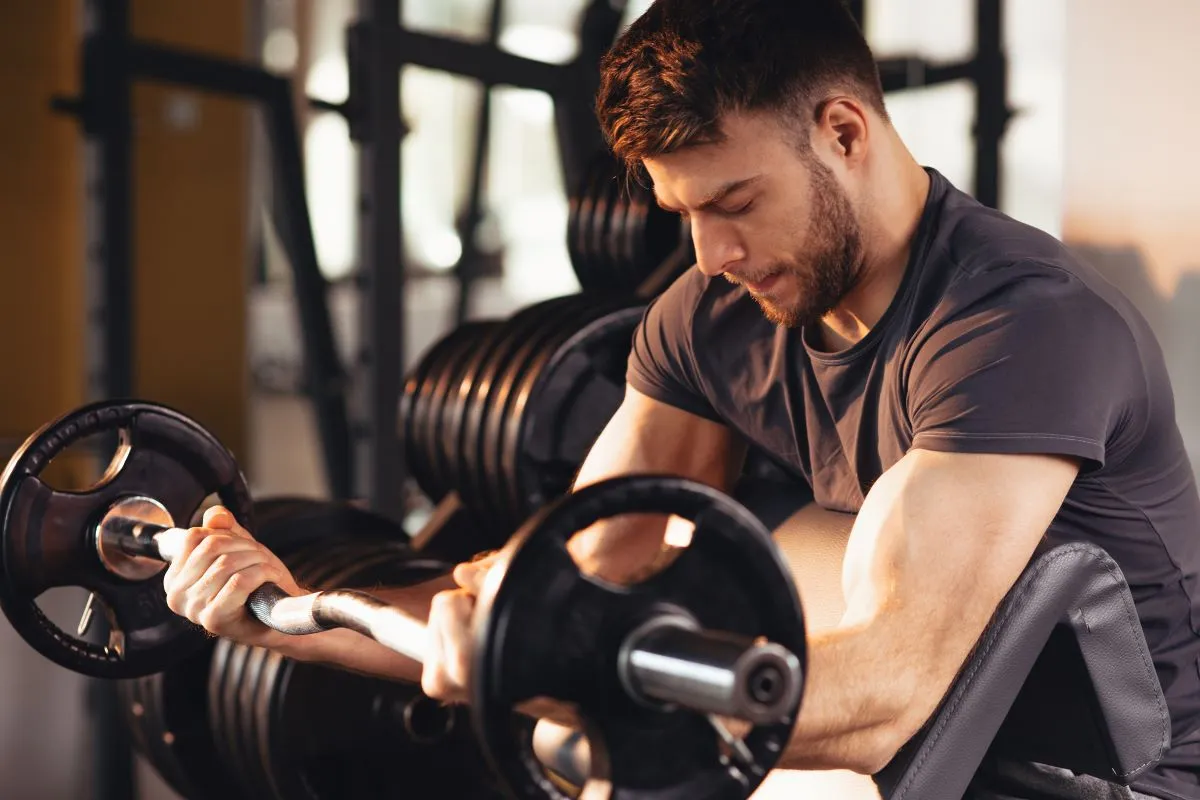 Férfi bicepszgyakorlatot végez rúddal az edzőteremben